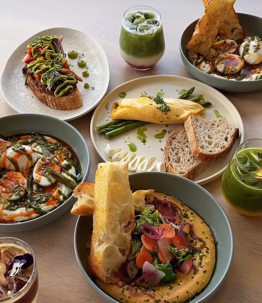 A brunch table: shakshuka, an omelette with asparagus, hummus with pickled vegetables, sourdough and iced matcha